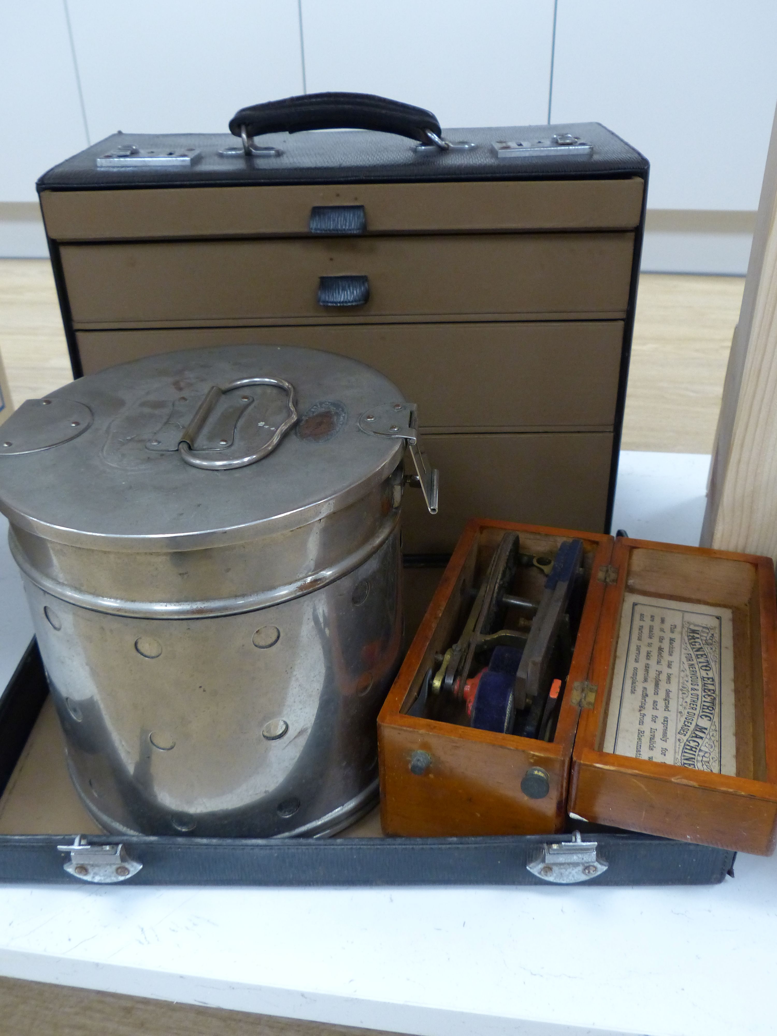 A leather cabinet case containing doctors equipment, a circular plated container, a wooden case and a magneto electric machine